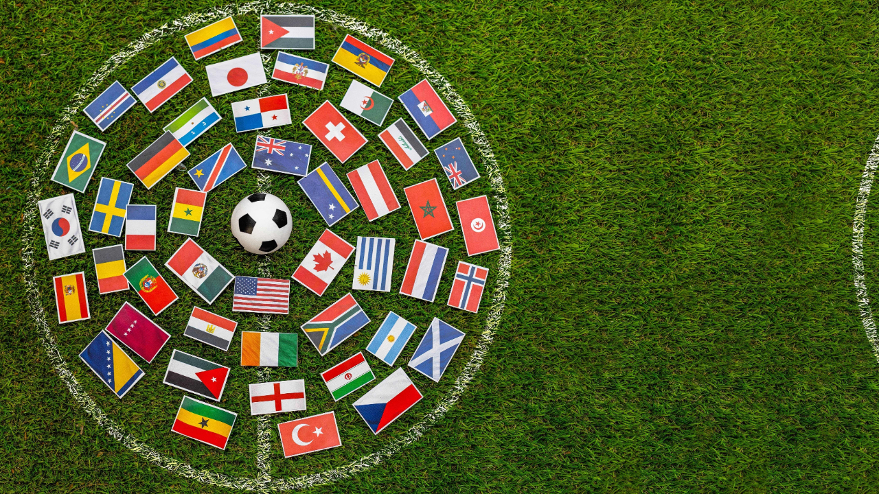 Balón de fútbol en el centro de una cancha rodeado por banderas de selecciones nacionales que simbolizan el Mundial 2026