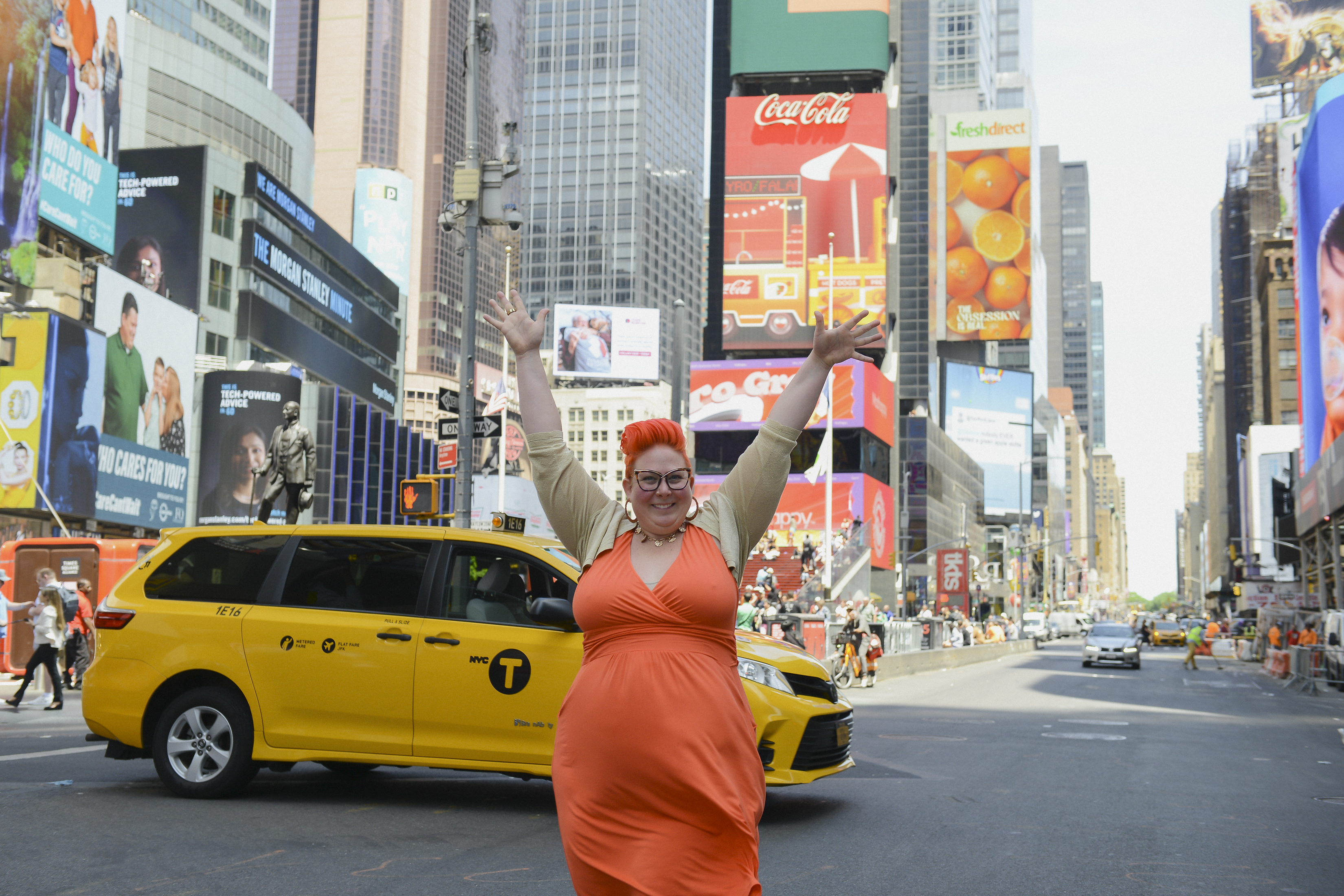 Jacquie in an orange dress, arms up in Times Square