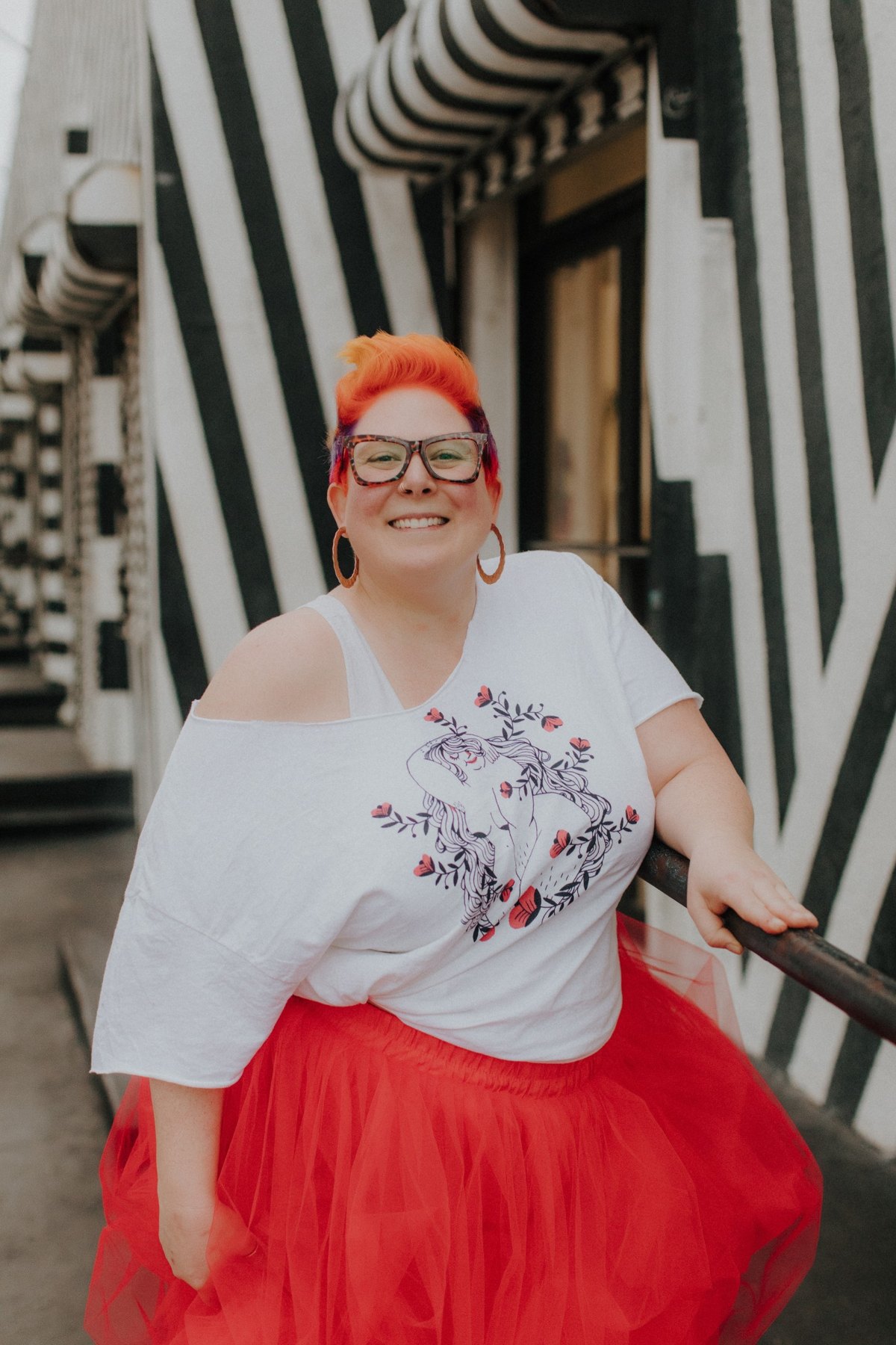 Jacquie in a red tulle skirt and white tee, laughing in front of a black-and-white striped wall