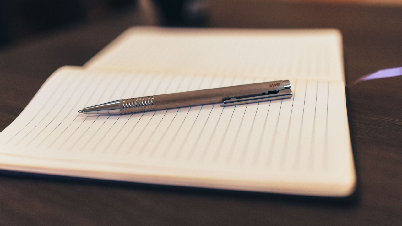 A worn leather notebook and pen on a wooden desk with a ceramic coffee cup, soft natural light from a nearby window.