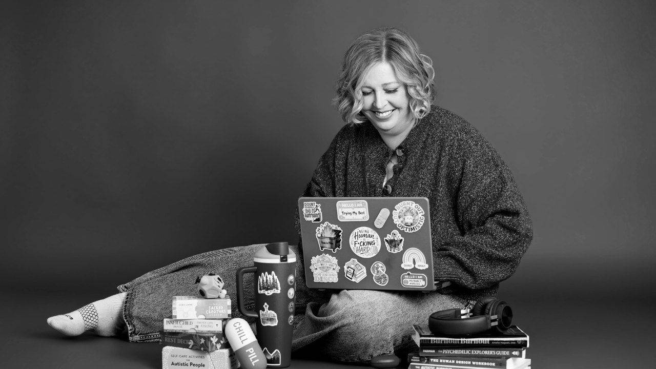 Therapist Becca Gerlach sitting on the floor with her sticker-covered laptop and a stack of books in a black and white portrait. When weekly therapy for burnout leaves you stuck, a burnout therapy intensive in Michigan gives your nervous system the uninterrupted time it needs to heal. Becca offers burnout intensives in Plymouth, Michigan, starting with a free consultation.