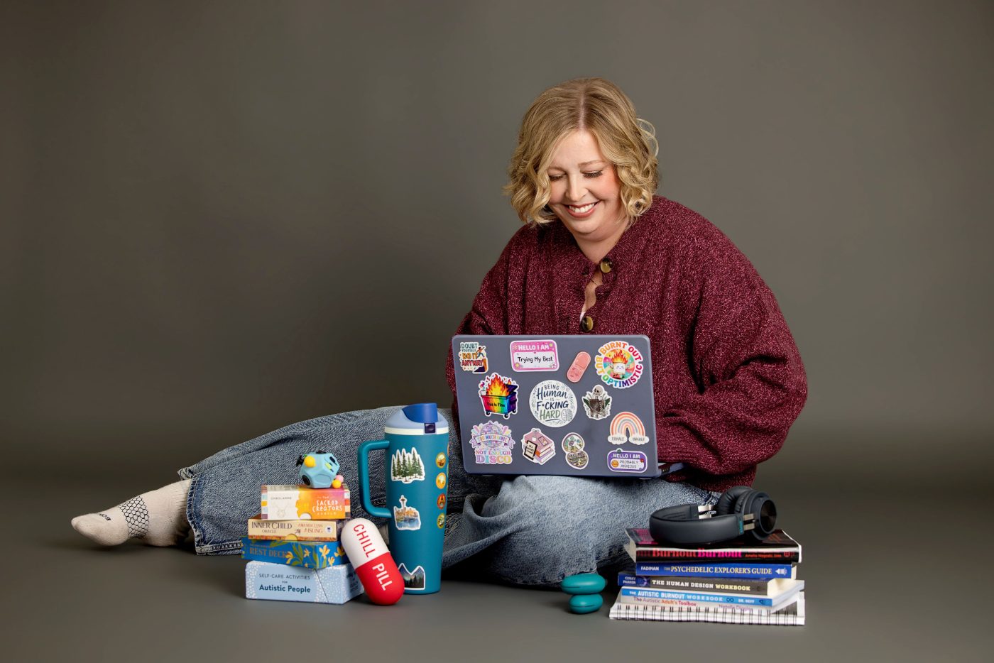Becca Gerlach sitting on the floor with a sticker-covered laptop, books, and a water bottle, ready for a burnout recovery therapy intensive