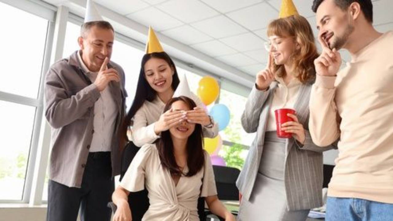 Woman in party hat surrounded by coworkers in surprise party.