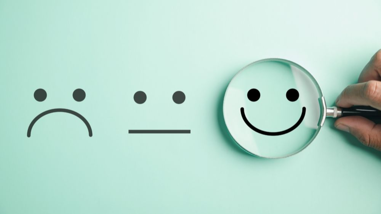 A hand holding a magnifier happy smiley face icon among other emotions.