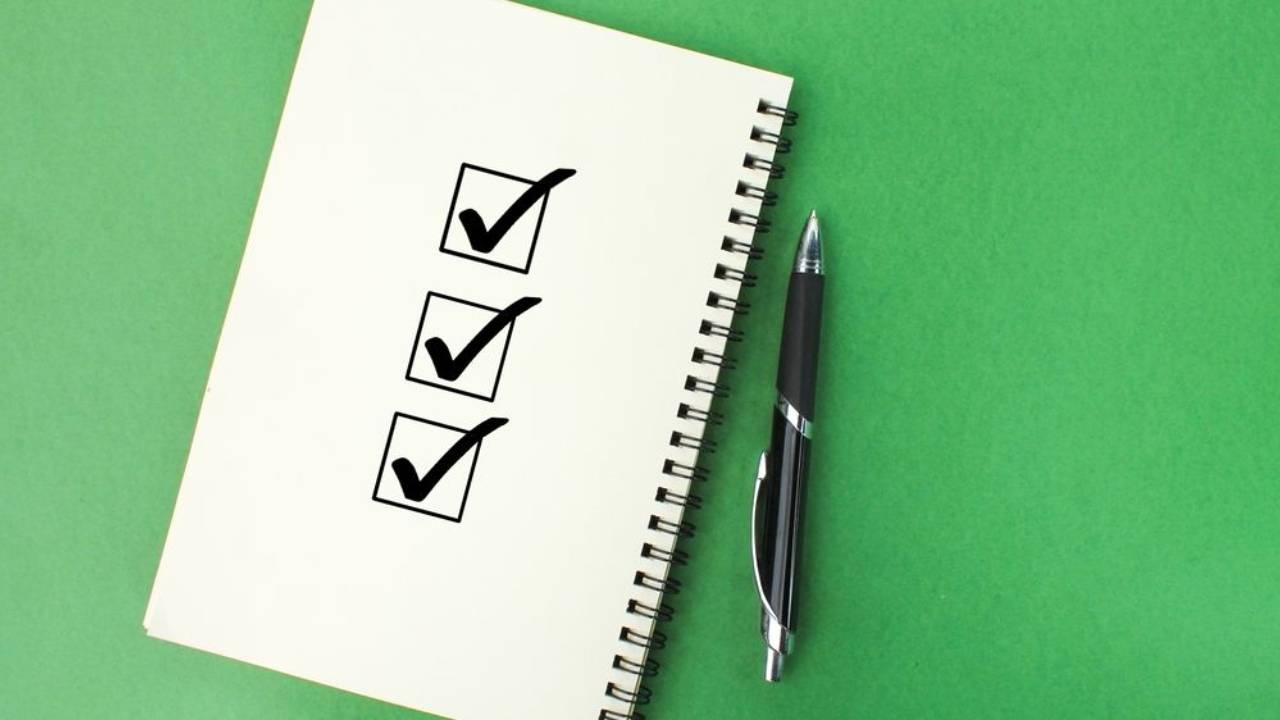 Notebook on green background with pen and 3 checkmarks on the open page.