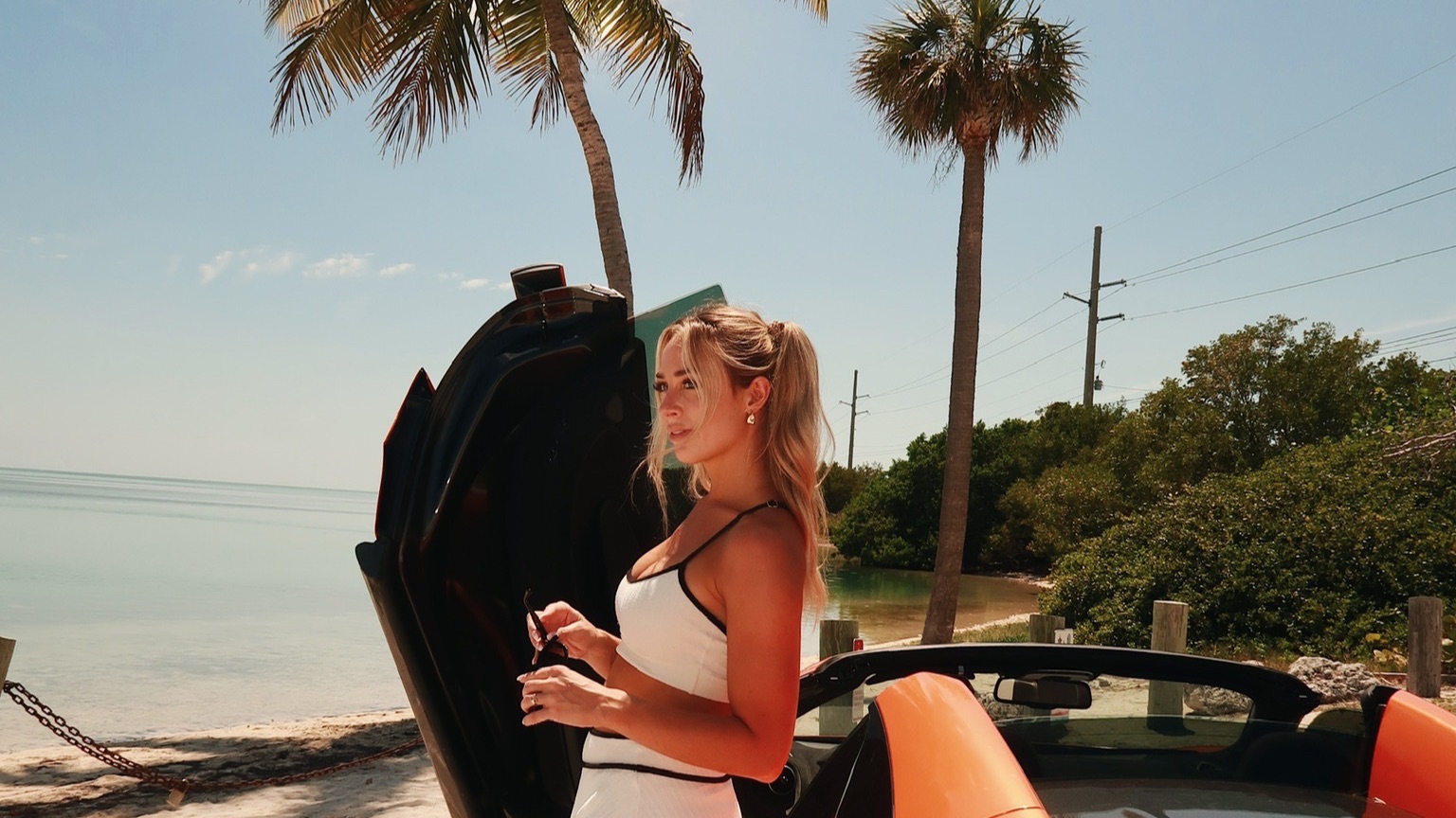 Brittany Arnason leaning against an orange sports car by the beach