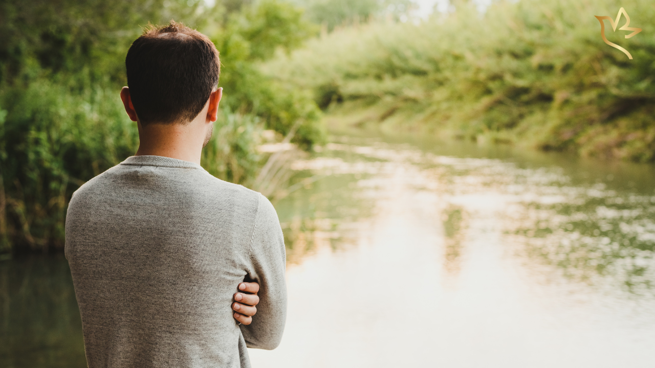 A man stands quietly beside a peaceful river, reflecting on healing, remembrance, and the gentle journey forward after the loss of a loved one.
