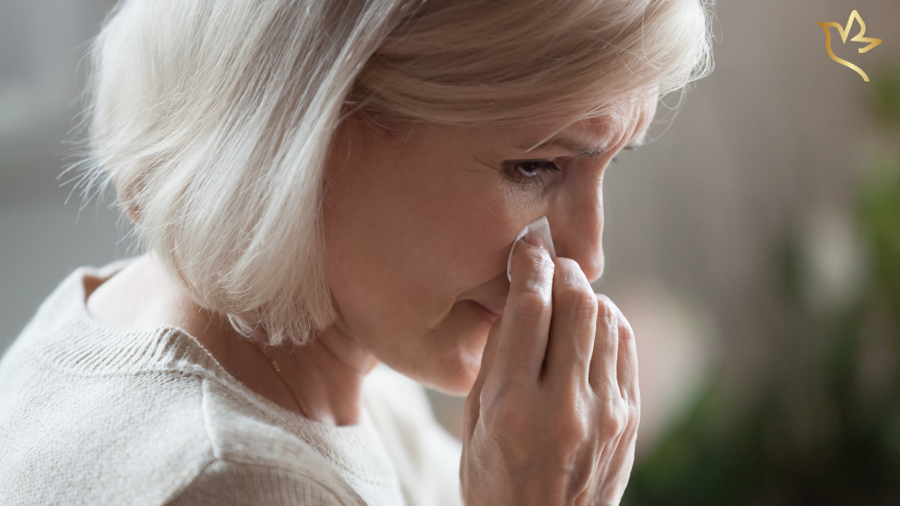 A grieving woman wipes away tears while searching for funeral assistance programs and financial help during a difficult time.