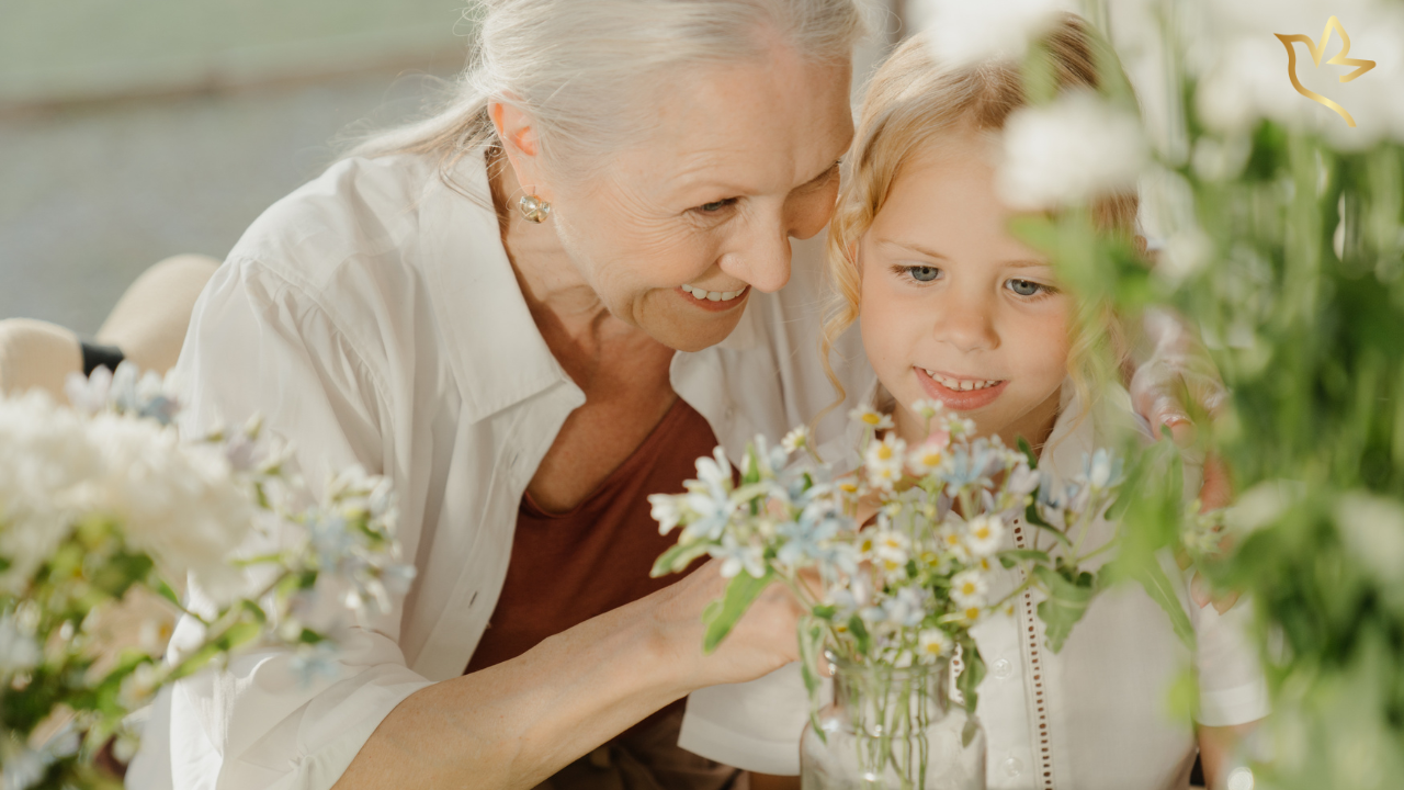 A grandmother and young granddaughter smile together while arranging fresh flowers, reflecting the quiet legacy of love passed from one generation to the next.