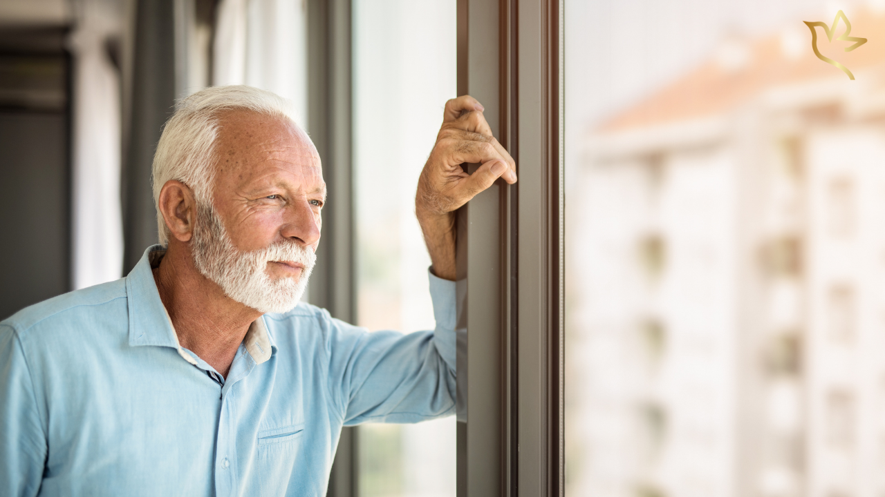 Older man looking thoughtfully out a window while considering what to do when a funeral fundraiser does not raise enough money.