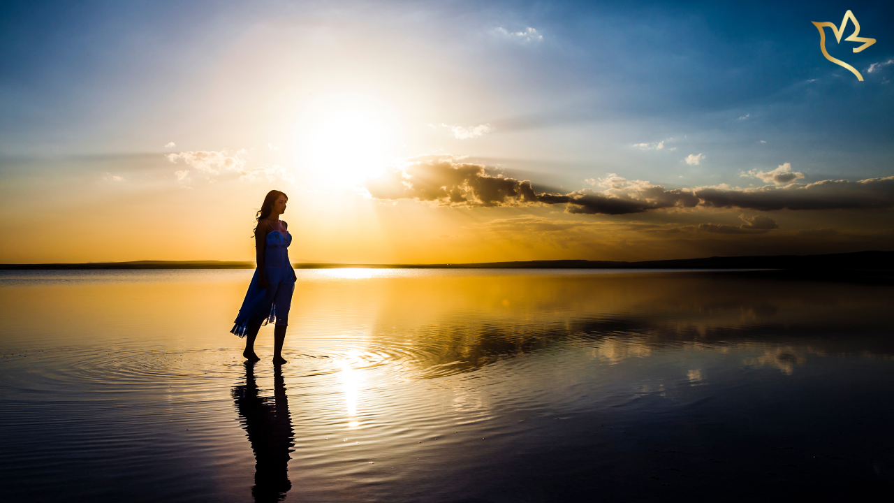 A woman stands barefoot in calm water at sunset, reflecting on healing, remembrance, and the quiet comfort found in meaningful rituals.