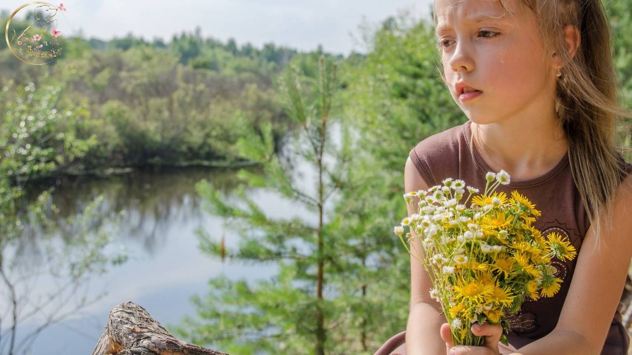 Young girl holding wildflowers while sitting beside a peaceful lake, reflecting quietly during a moment of grief and remembrance after the loss of a beloved pet.