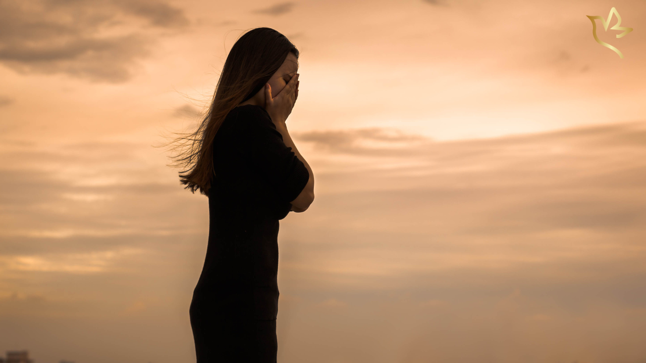 A woman stands quietly at sunset with her hands covering her face, reflecting on the unexpected emotions that small memories can awaken after the loss of a loved one.