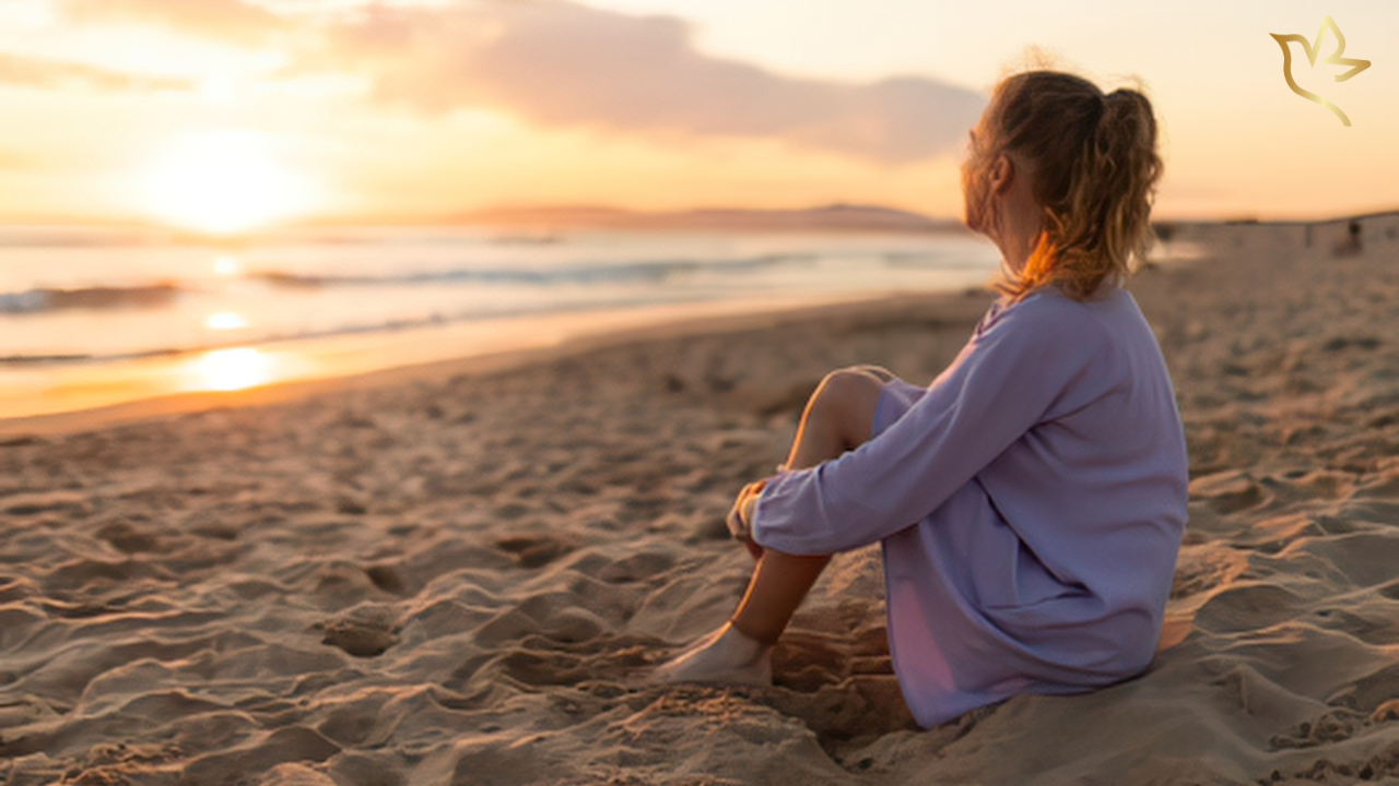 A young woman sits quietly on a sandy beach at sunset, looking toward the horizon as she reflects on love, remembrance, and the quiet strength found in cherished memories.