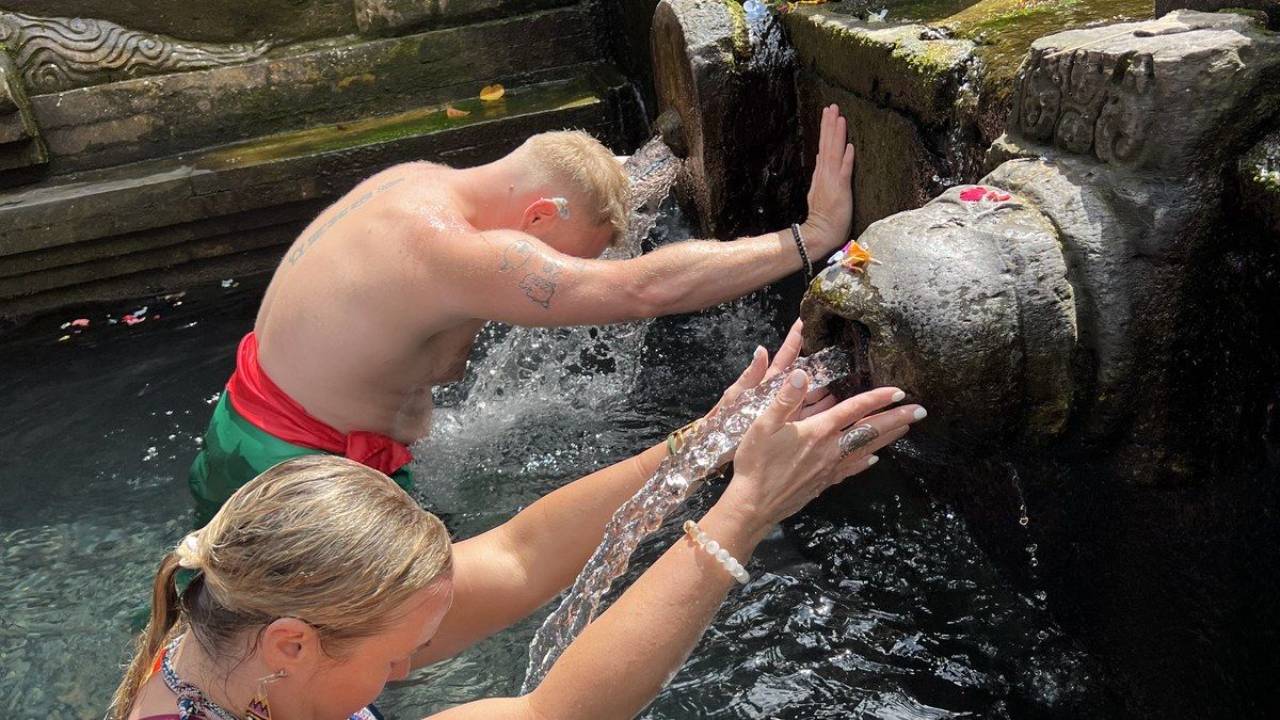 Two people practicing a water blessing ritual at a temple, hands reaching toward flowing water as part of calling in the light