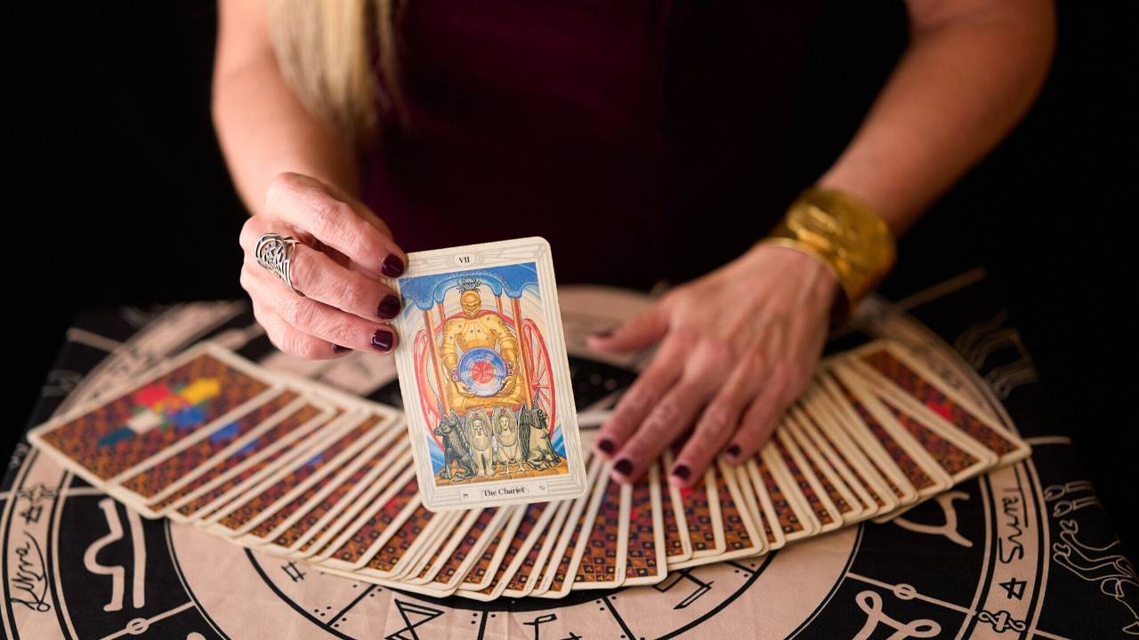 Hands holding a tarot card over a spread of tarot cards during a private psychic life coach reading