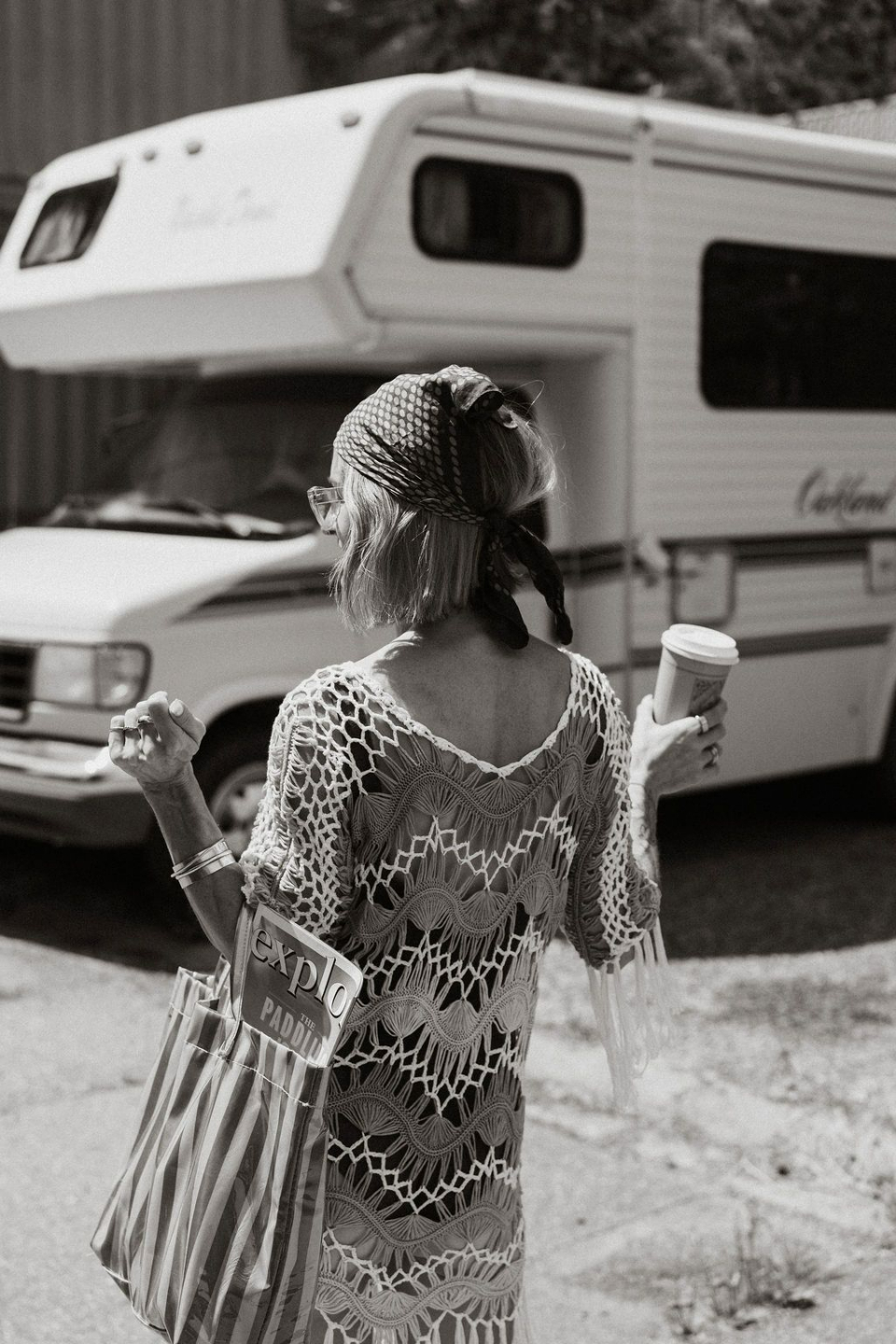 PLACEHOLDER — B&W photo: walking past vintage RV with coffee
