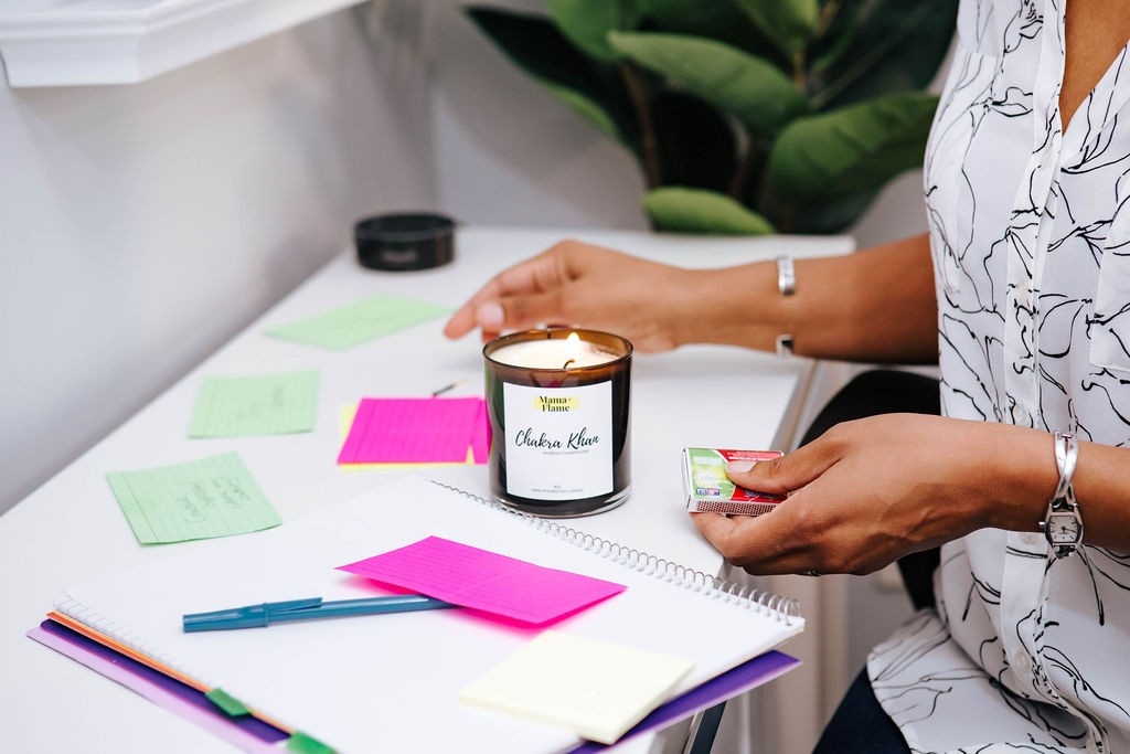 The arms of a woman lighting a candle on her desk alongside a notebook and index cards.