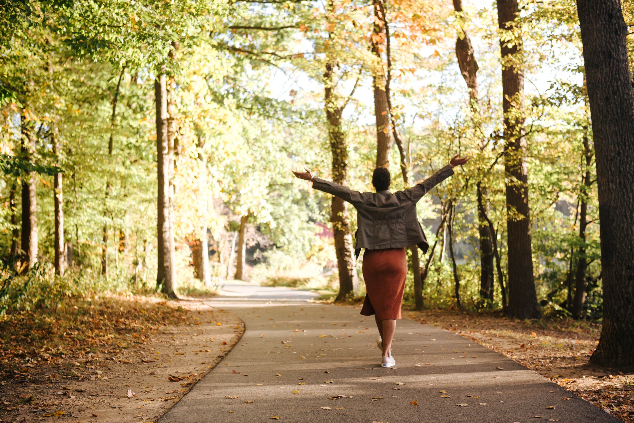 Woman walking through a path surrounded by nature, with her spread wide