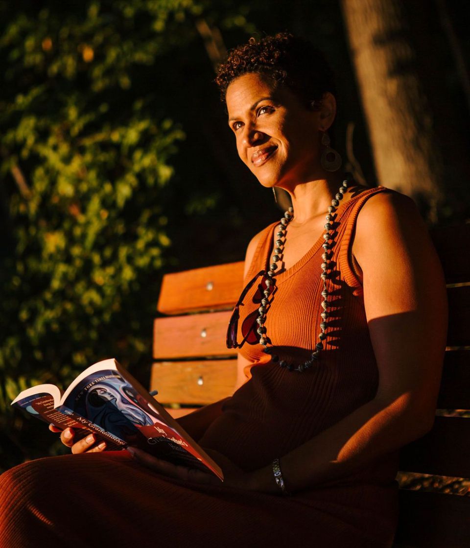 Woman sitting down on a bench, with a book in her hands, and staring off into the distance.