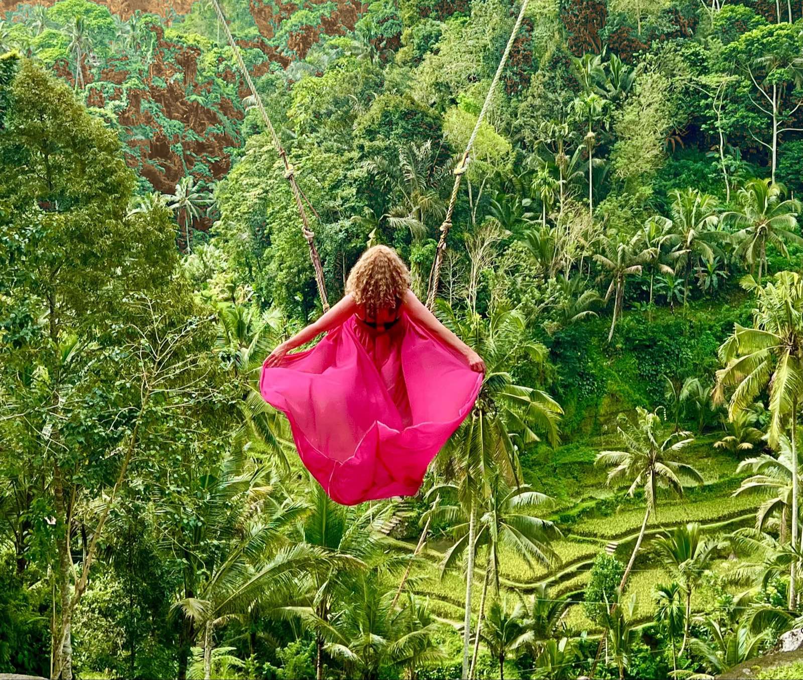 A woman in a flowing pink dress on a jungle swing — free, alive, joyful