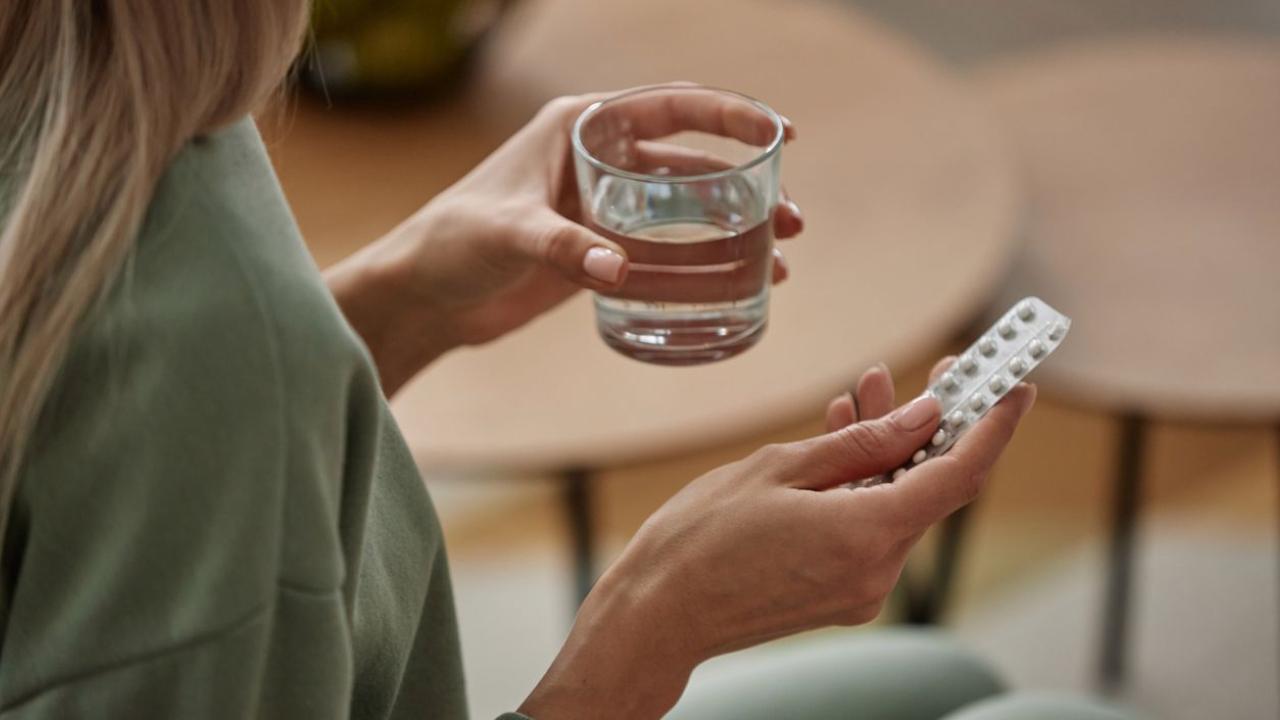 woman with a green shirt holding a glass of water and birth control