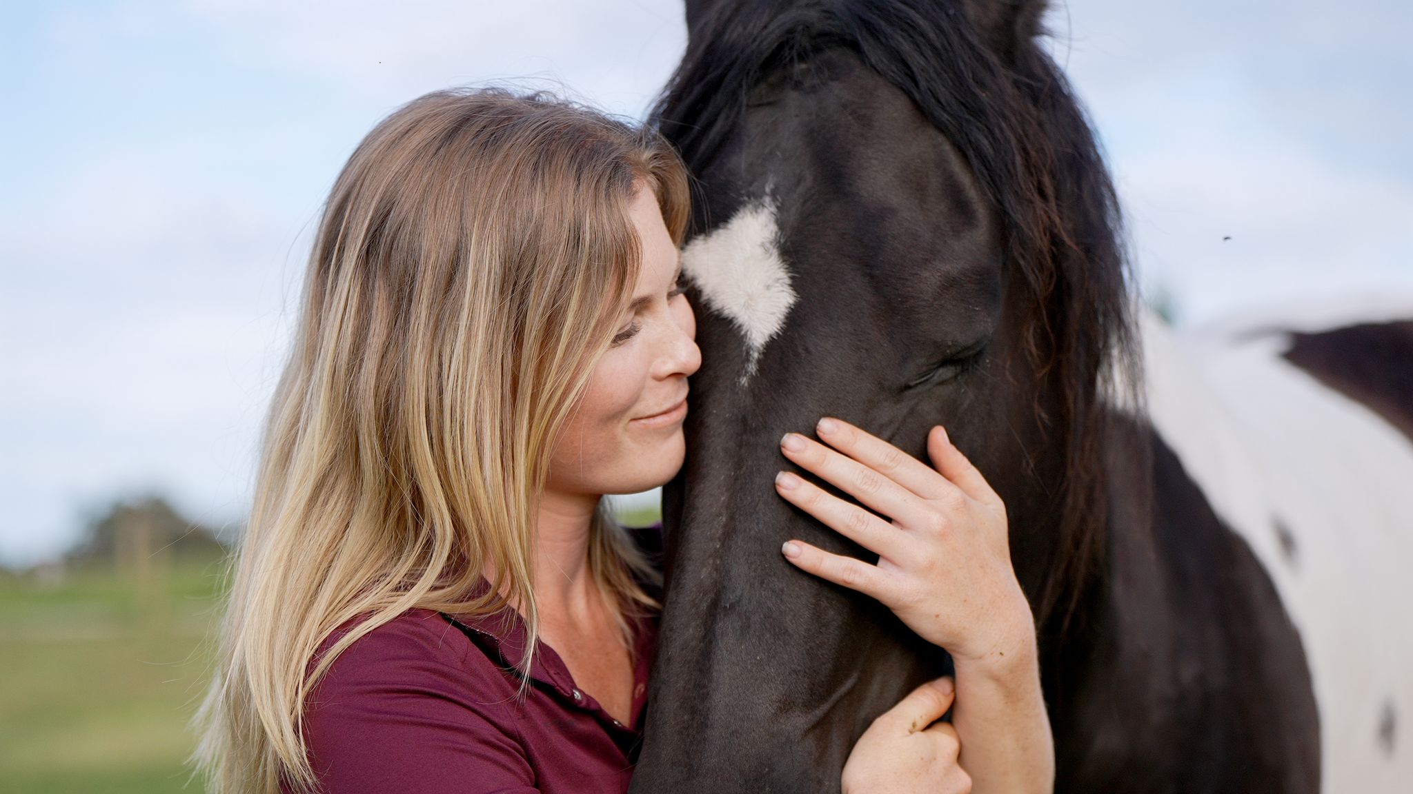 Nadine resting her face against a black and white horse&rsquo;s forehead, her hand on his cheek
