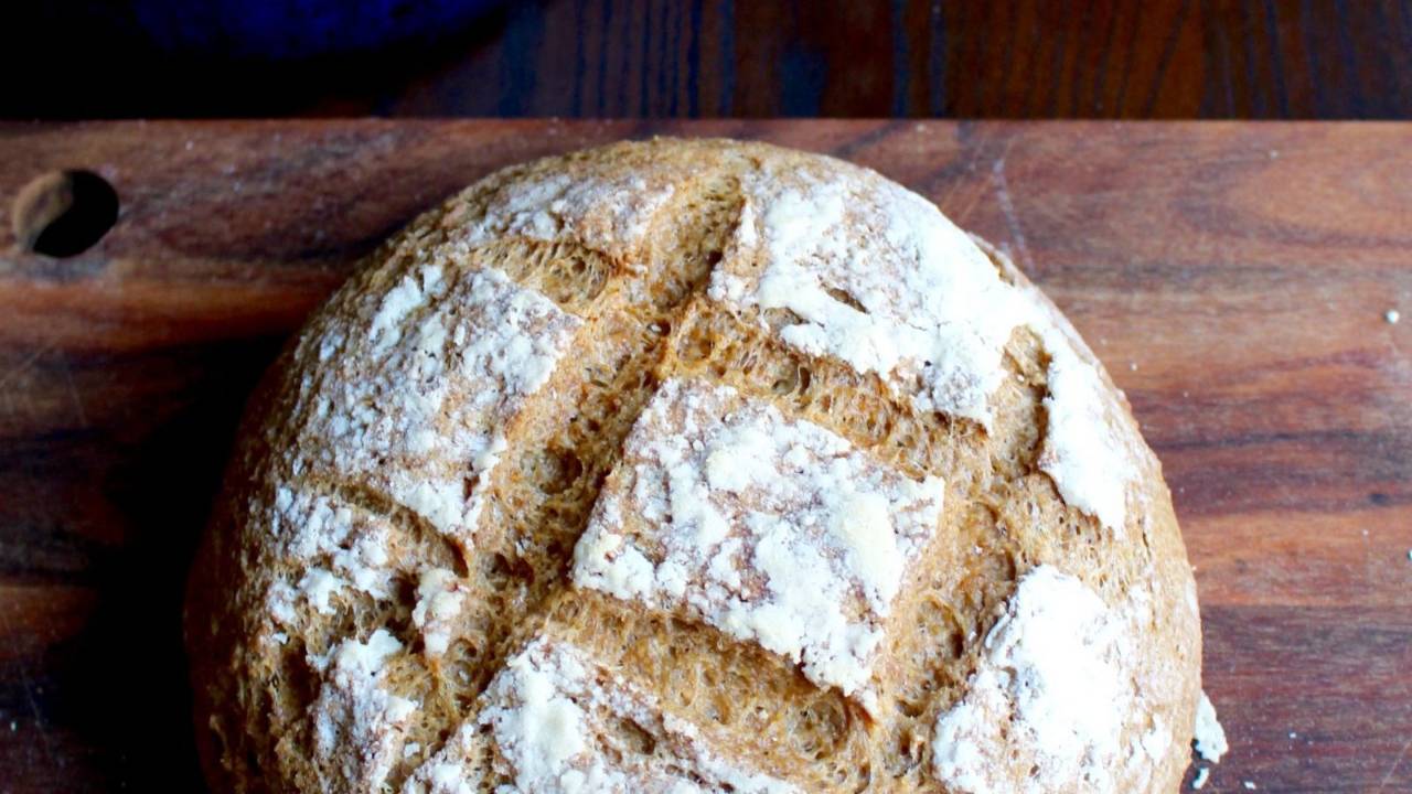 Glutenfritt bröd på en träskärbräda bredvid en blå gryta