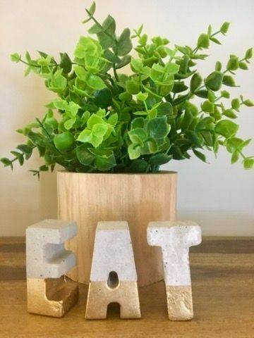 Decorative photo of wooden "EAT" letters on a shelf with a potted plant, representing a mindful, nourishing approach to food