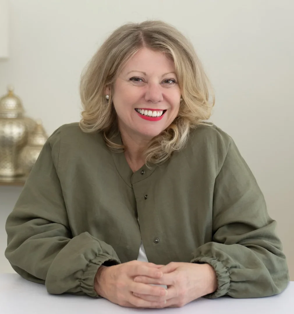Deb Szabo, AI business strategist, smiling at her desk in an olive jacket