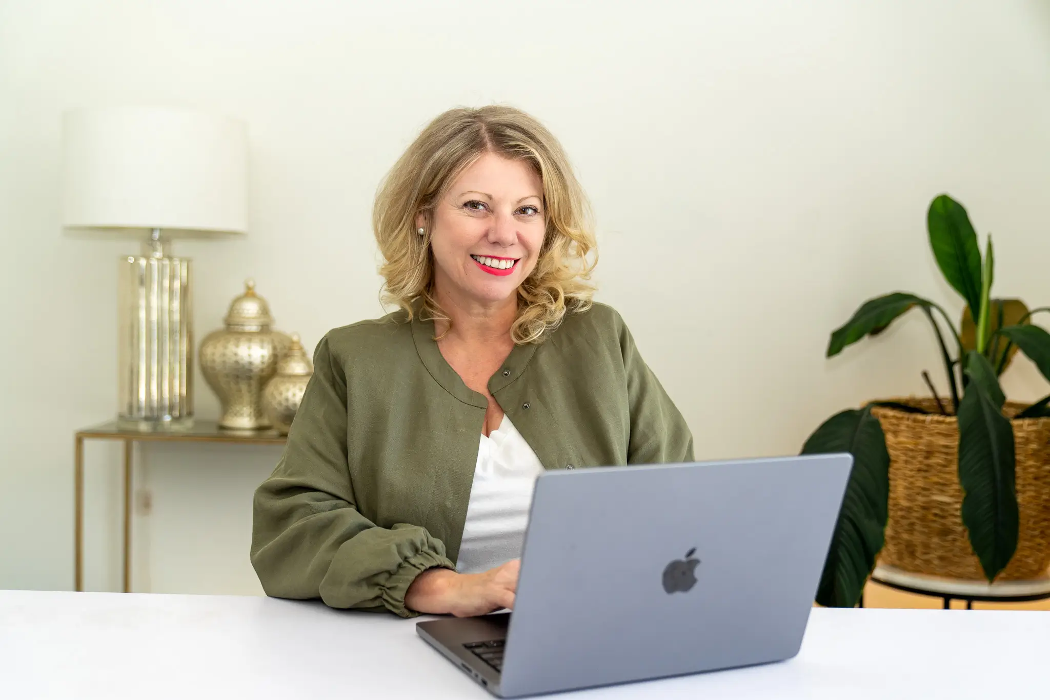 Deb Szabo, AI Business Strategist, working on a MacBook in an olive jacket