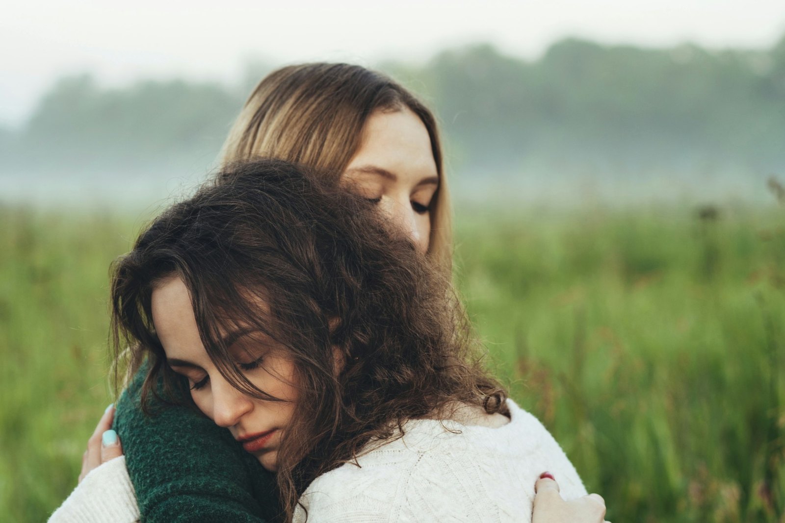 Two women holding each other in a warm embrace in a misty field