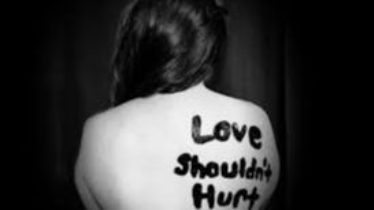 Woman with words "Love Shouldn't Hurt" written on her back representing the hidden pain of coercive control and emotional abuse