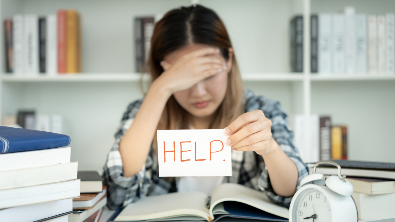 Picture of woman looking overhwhelmed holding sign with "help" written on it.