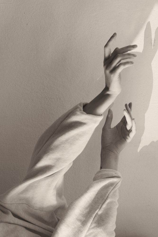 Two hands reaching up a sunlit wall