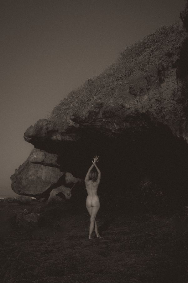 Rachel beneath a sea cliff, arms raised