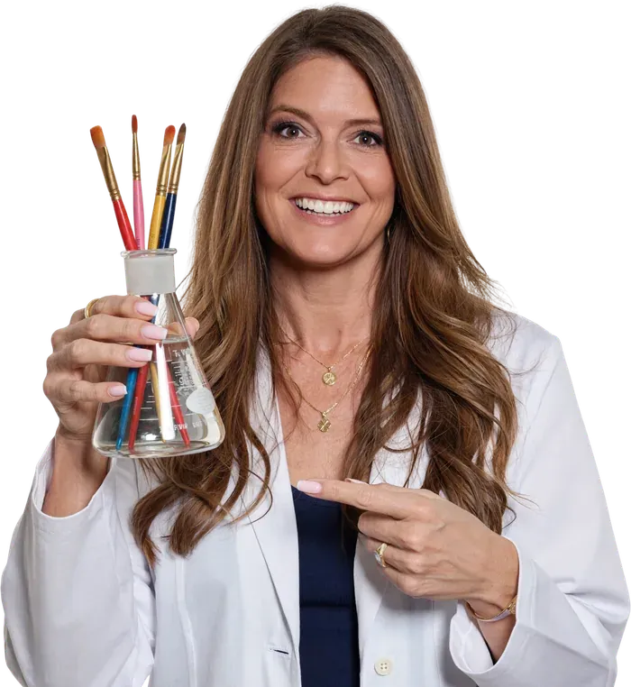 Mandy Corcoran in a lab coat holding a flask of paintbrushes, Creative Systems Lab by Amanda Grace Design