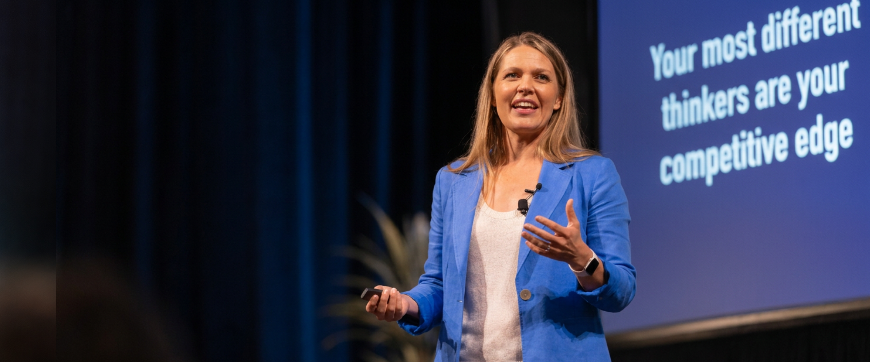 Mariane Power speaking on stage beside a slide reading: Your most different thinkers are your competitive edge