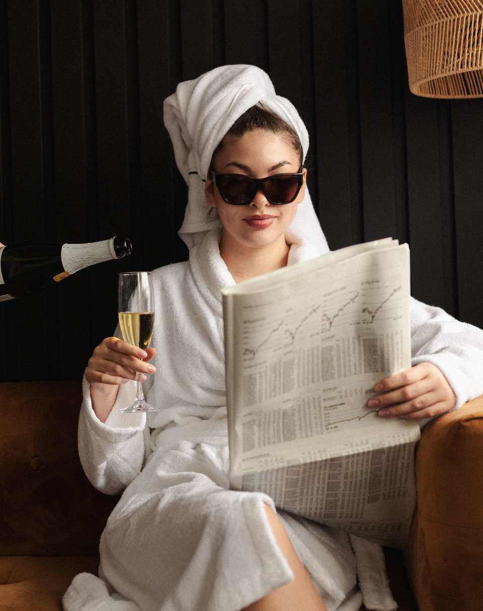 Bride in a robe and sunglasses with a glass of champagne and the newspaper
