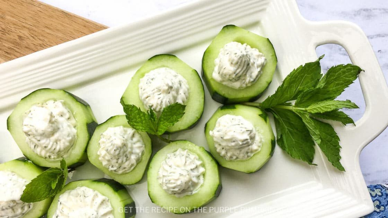 Round English cucumber slices laid flat on a white serving plate, each topped with a dollop of white cottage cheese and green dill.