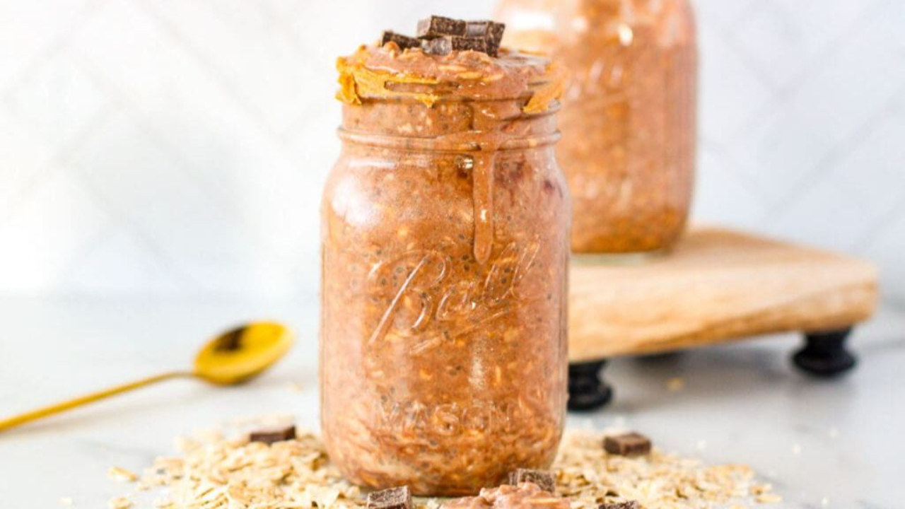 Layered chocolate protein overnight oats in a glass mason jar topped with a spoonful of natural creamy peanut butter and chia seeds.