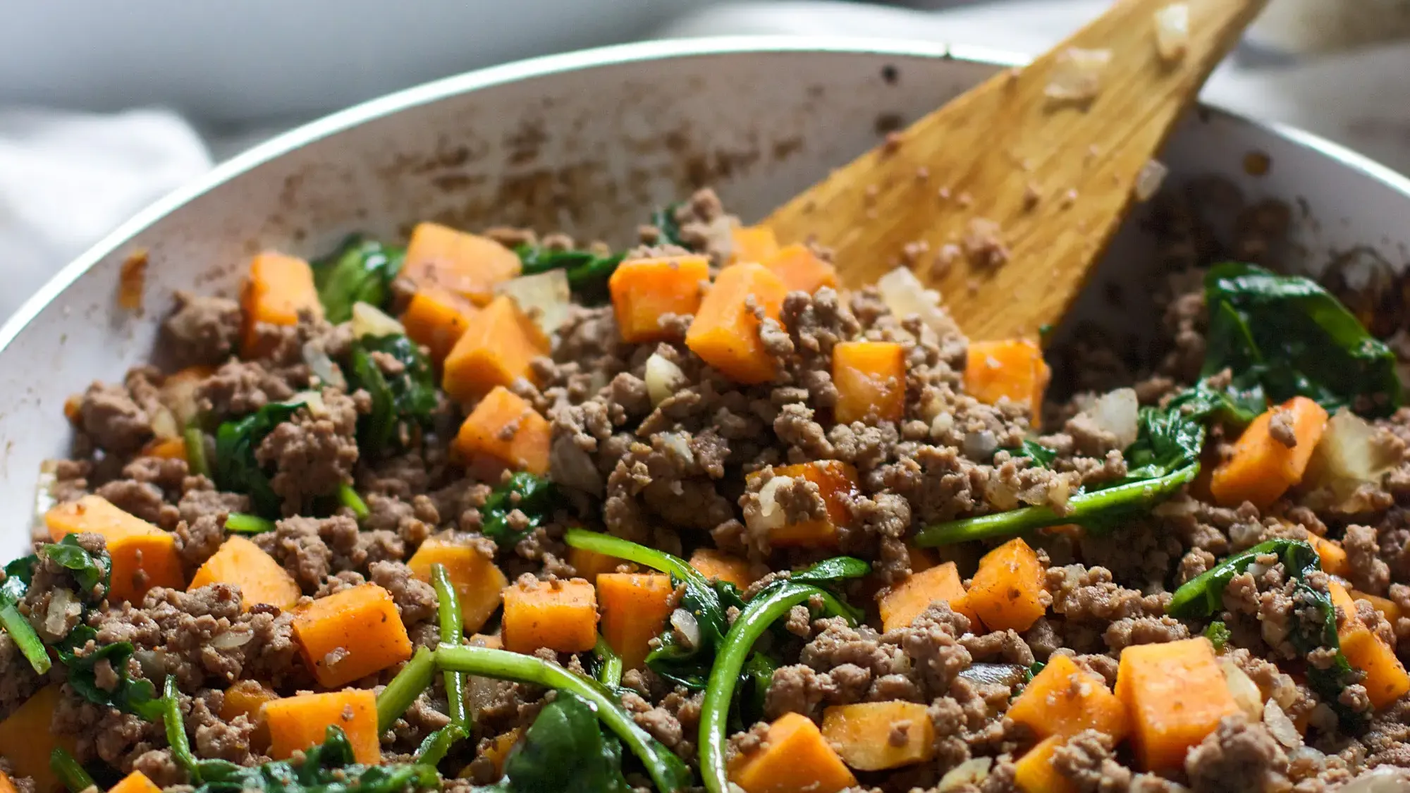 Ground beef skillet stir-fry with small cubes of roasted orange sweet potato, yellow onions, and fresh green spinach leaves.