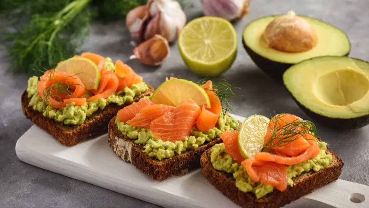 A thick slice of toasted whole-grain bread topped with mashed green avocado, folded smoked salmon slices, and red pepper flakes.