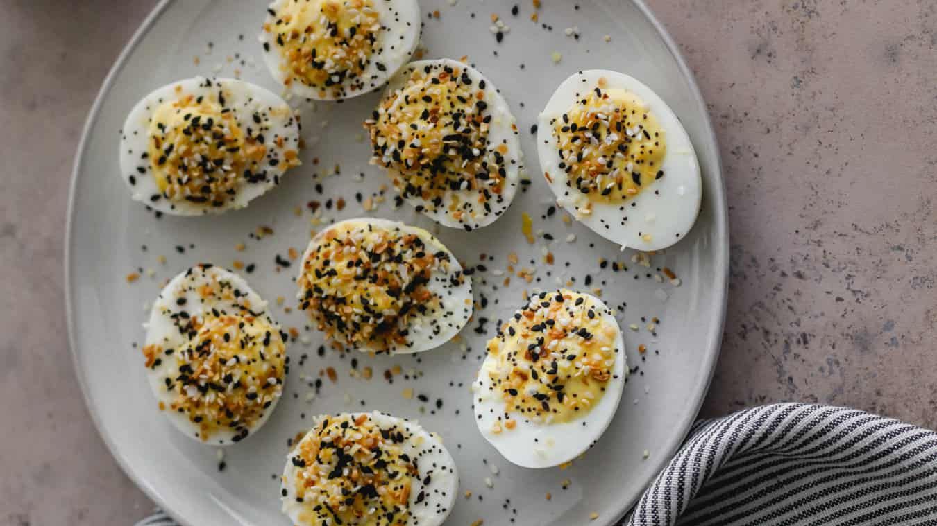 Four hard-boiled egg halves arranged yolk-side up on a small snack plate, heavily dusted with everything bagel seasoning.