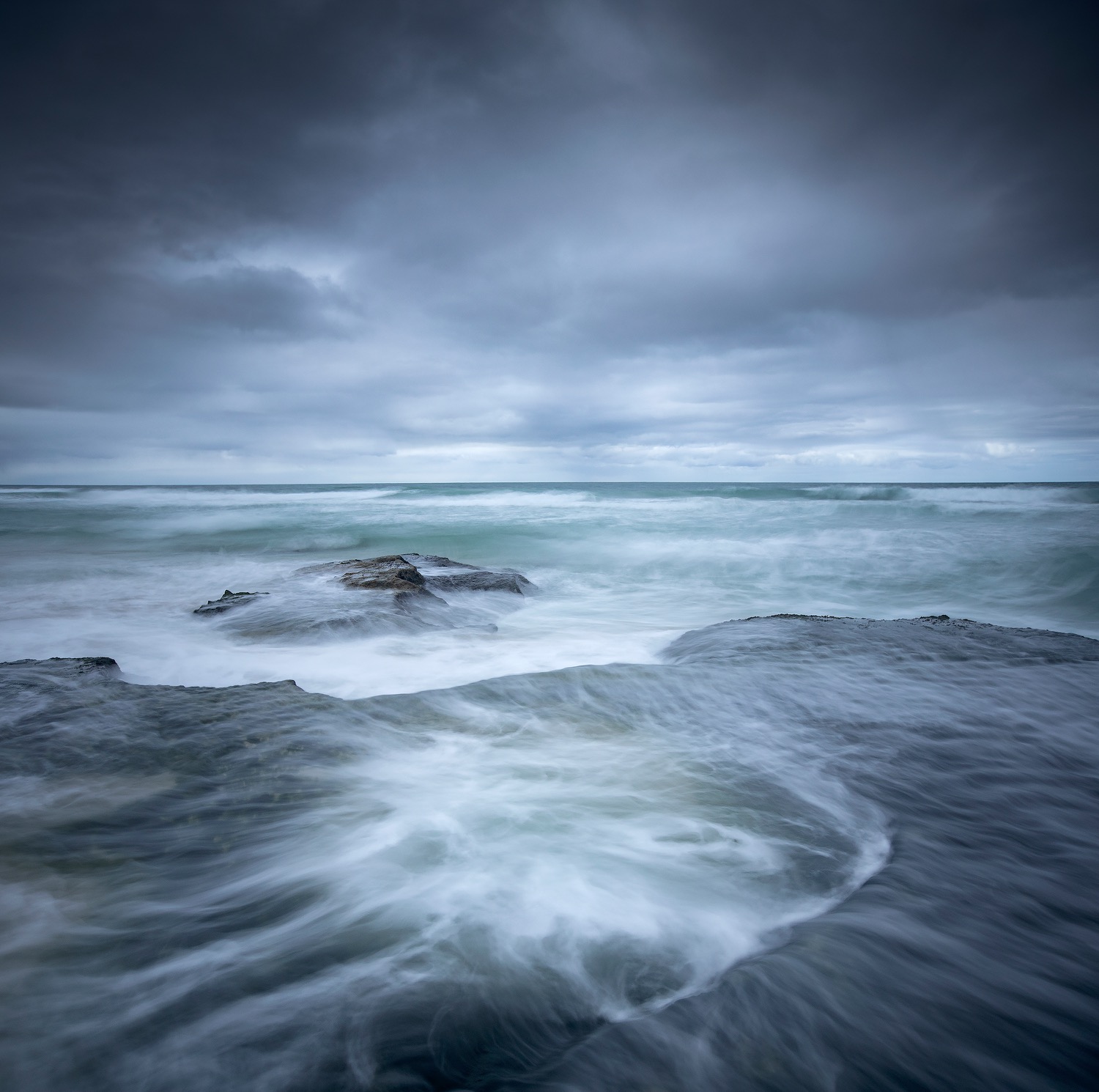 Blue long exposure of the sea washing over a low rock shelf at dusk on the Southern Cape coast
