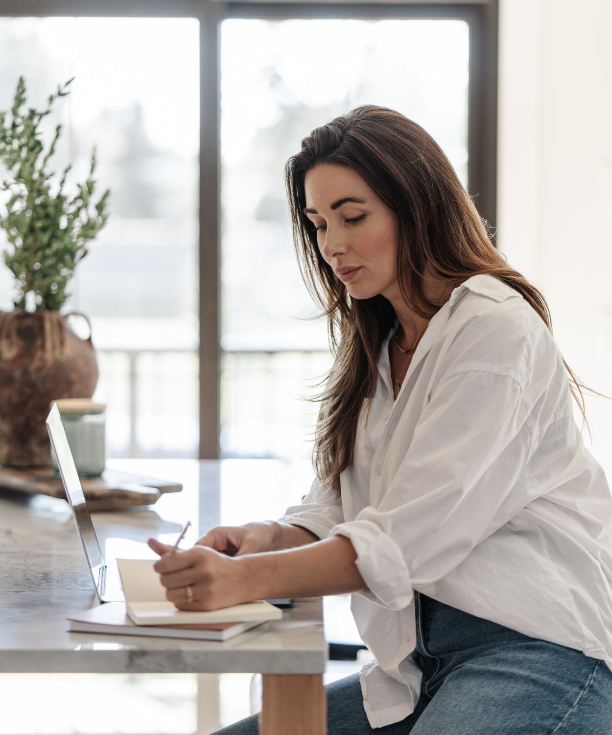 A woman working alone at her desk, notebook and laptop open