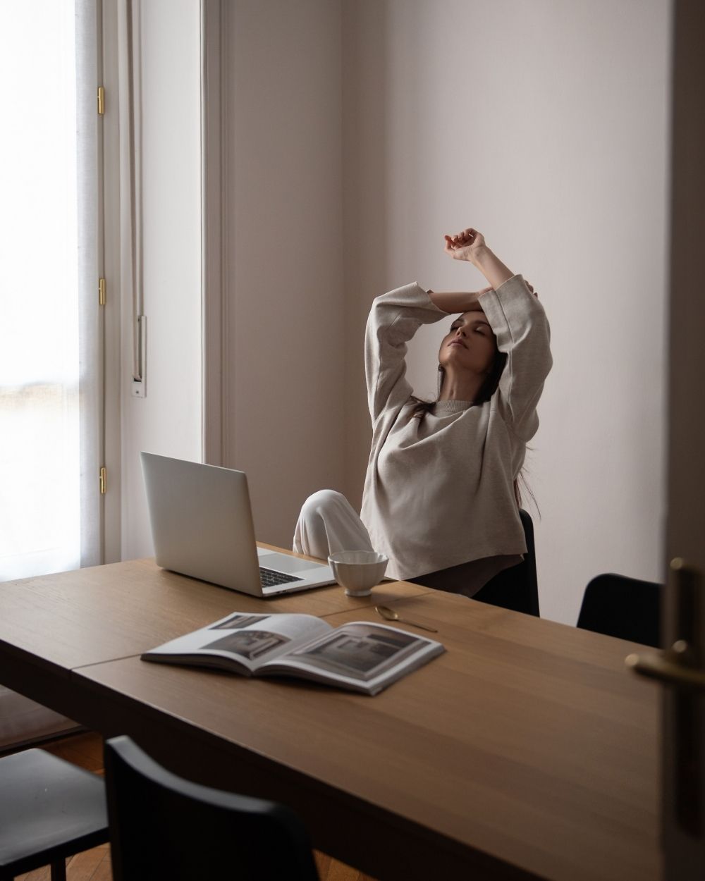 Business owner stretching back from her laptop after another long stretch of work.