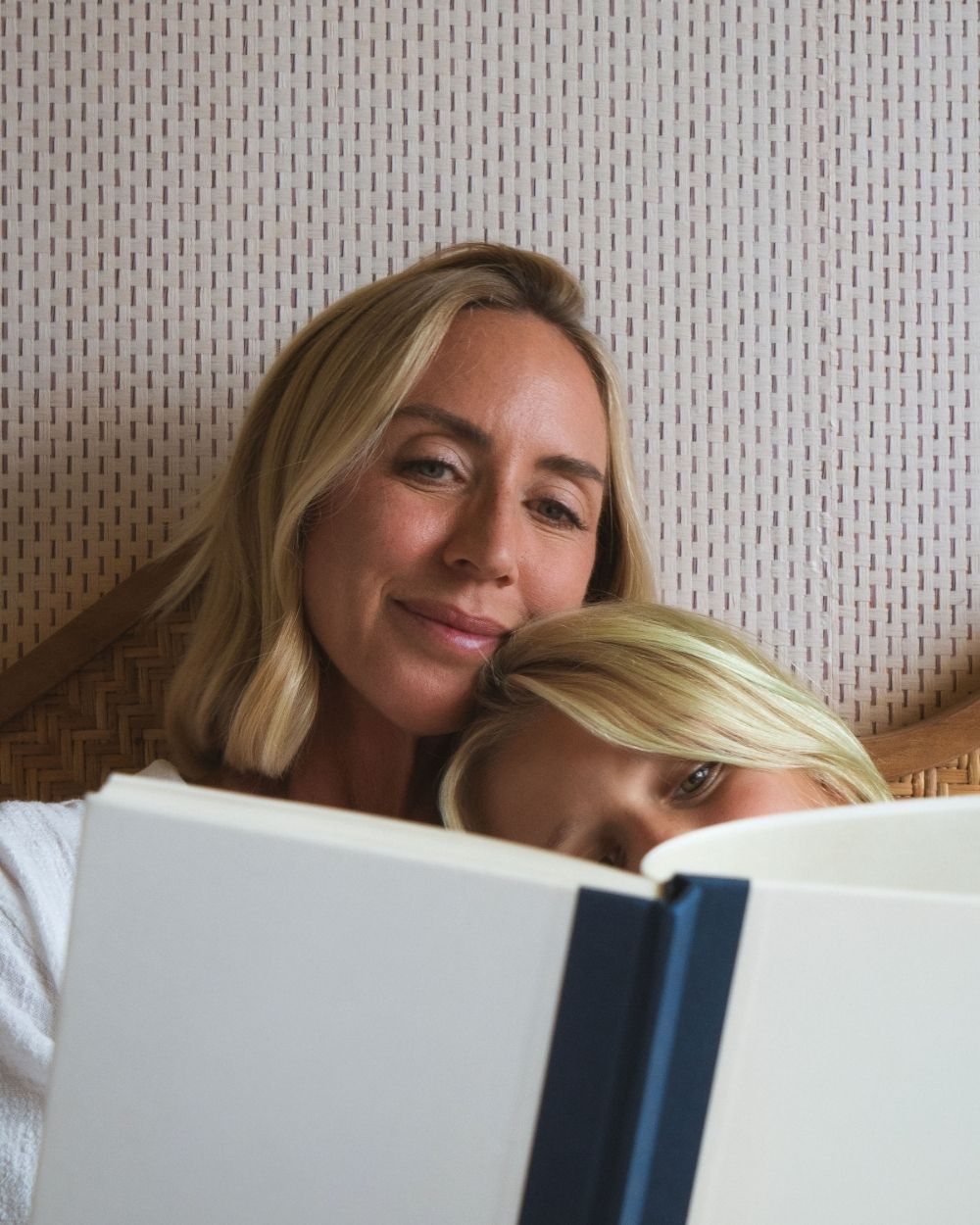 A mother and her young child reading a book together, cheek to cheek.