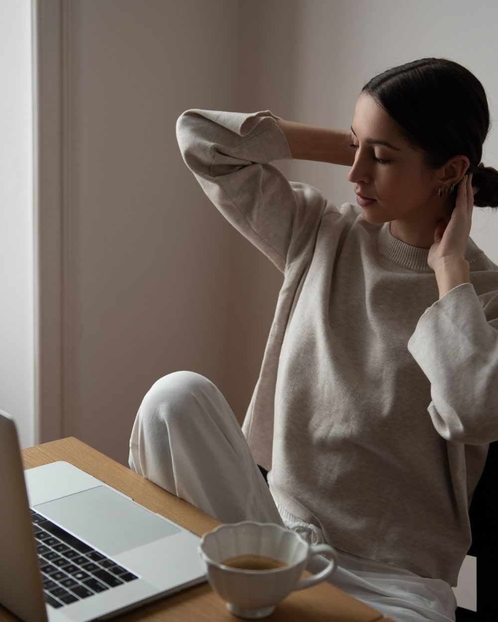 A woman pausing at her laptop with a cup of coffee, eyes closed, taking a breath.
