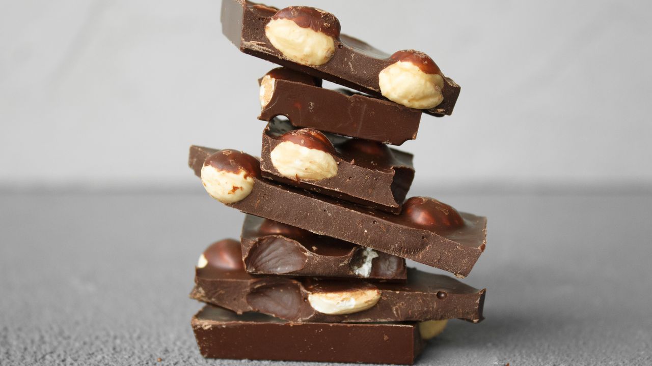 Stack of broken dark chocolate pieces studded with whole hazelnuts on a grey stone surface